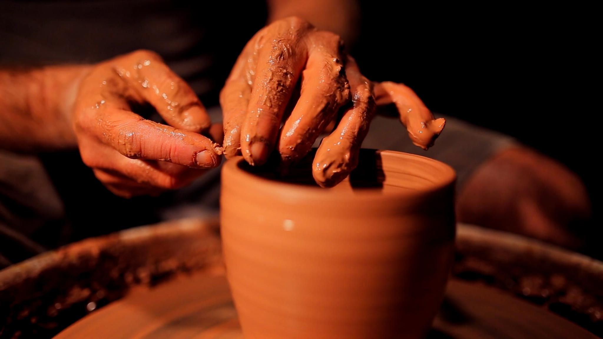 Close-up of hands molding clay on a pottery wheel in ambient lighting.